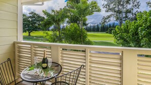 Un balcon avec une table et des chaises, donnant sur un terrain de golf bordé d’arbres et surplombant un ciel nuageux.