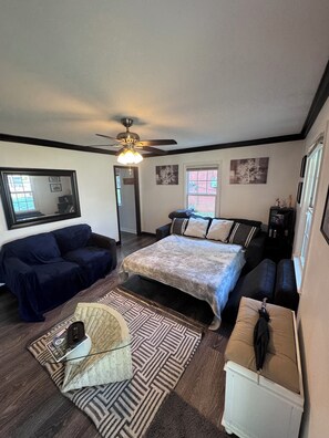 A bedroom with a bed, two sofas, a ceiling fan, and a window. - Small Brick Beauty (Charlotte)