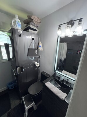 A compact bathroom with a toilet, a small step stool, a sink with a mirror, and a towel rack. - Small Brick Beauty (Charlotte)