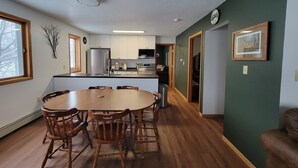 A modern kitchen with white cabinets, a stainless steel refrigerator, and a dining area with a wooden table and chairs. - LAKEFRONT 3-bedroom Chateau Getaway at Whitecap Mountains Resort Unit 2 (Upson)