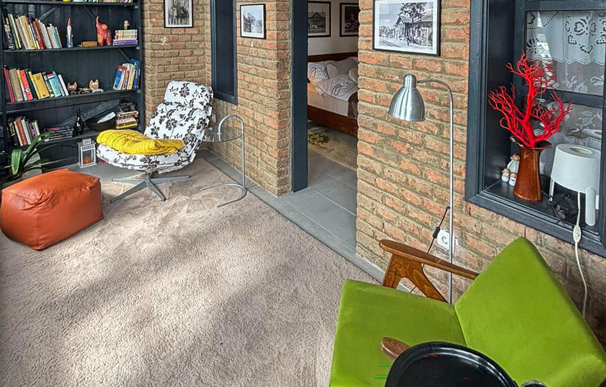 A cozy living room with a green sofa, a yellow chair, a red pouf, and a bookshelf filled with books.