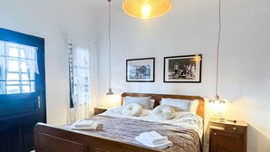 Ein Schlafzimmer mit einem Bett, zwei Nachttischen, einer Pendelleuchte, einer Tür und zwei gerahmten Bildern an der Wand.