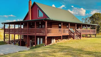 A large, two-story log cabin with a green roof and a porch.