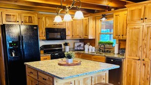 A kitchen with wooden cabinets, a black refrigerator, a microwave, a stove, and a sink. There are two stools at the island.
