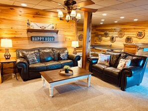 A cozy room with a leather sofa, a coffee table, and a wooden wall with various signs. - The Bourbon Lodge - Log cabin and Bourbon Trail! 🥃 (Springfield)