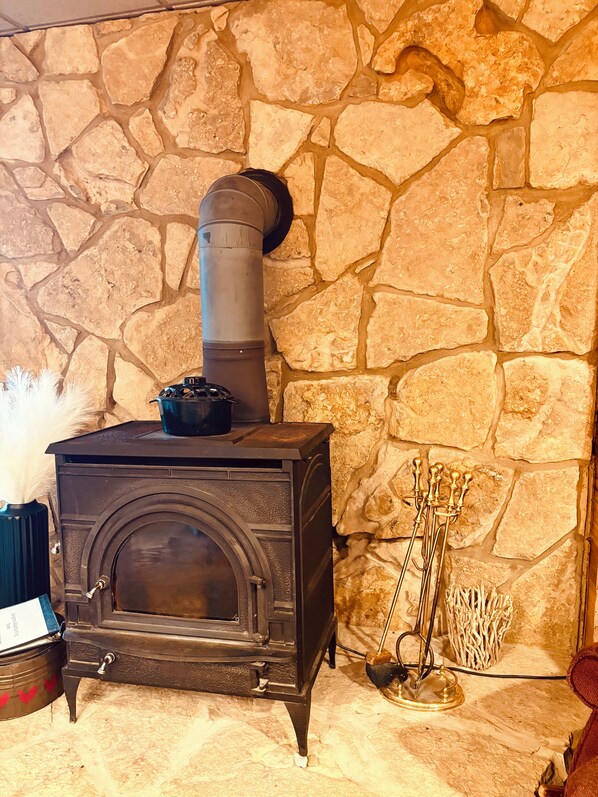 A stone wall with a wood-burning stove, a metal pot on top, and a broom leaning against the wall.