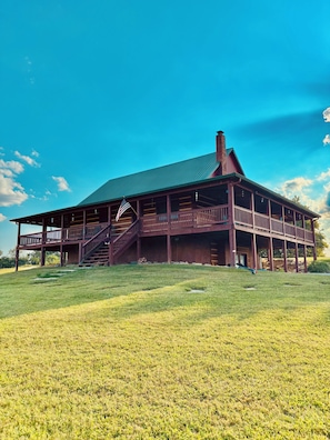 A large wooden building with a green roof, a staircase leading to a porch, and an American flag.