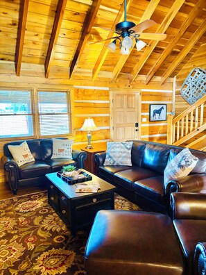 A cozy log cabin interior with a leather sofa, a coffee table, and a ceiling fan.