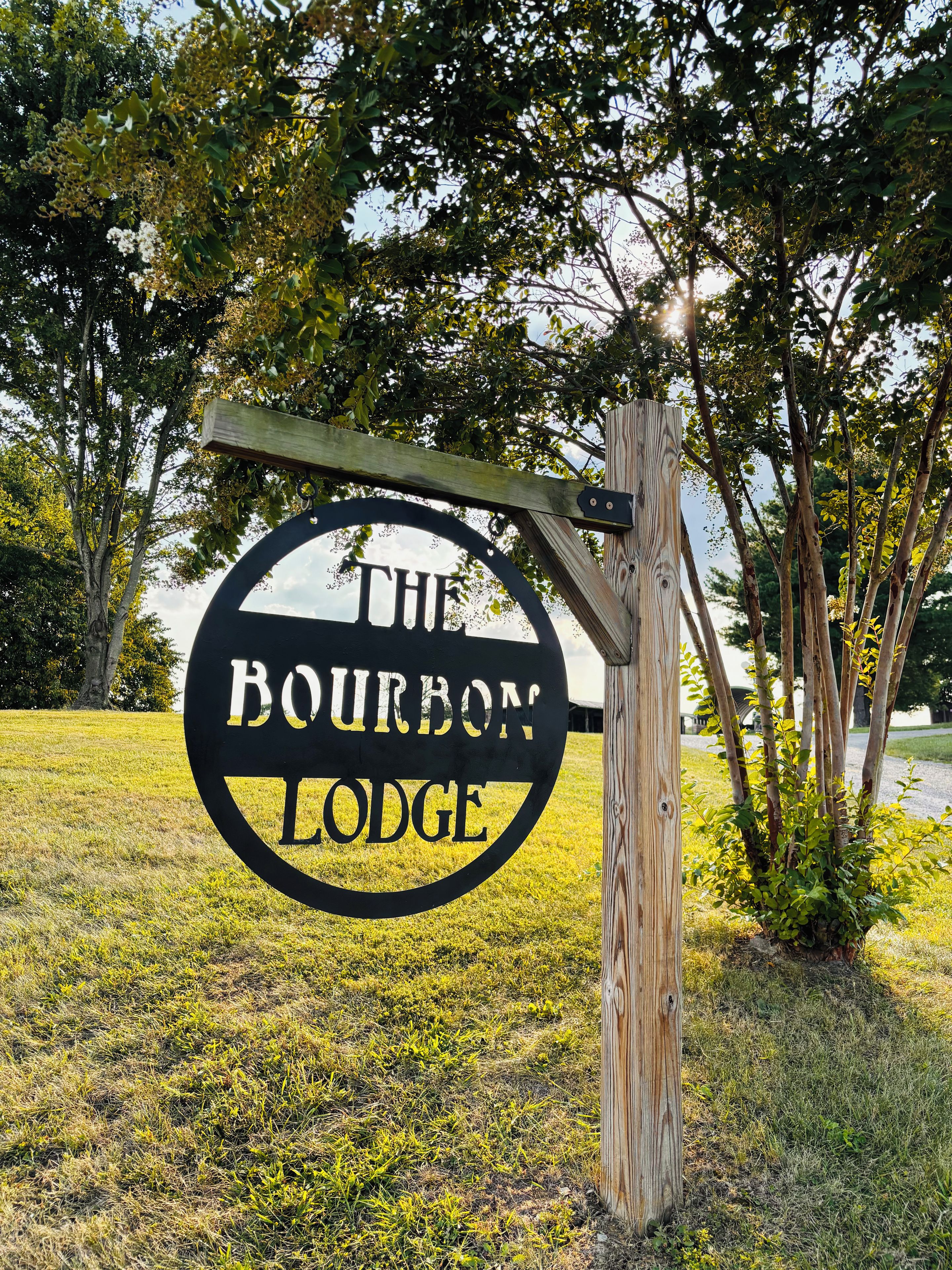 Um sinal circular com o texto 'THE BOURBON LODGE' fixado em um poste de madeira.