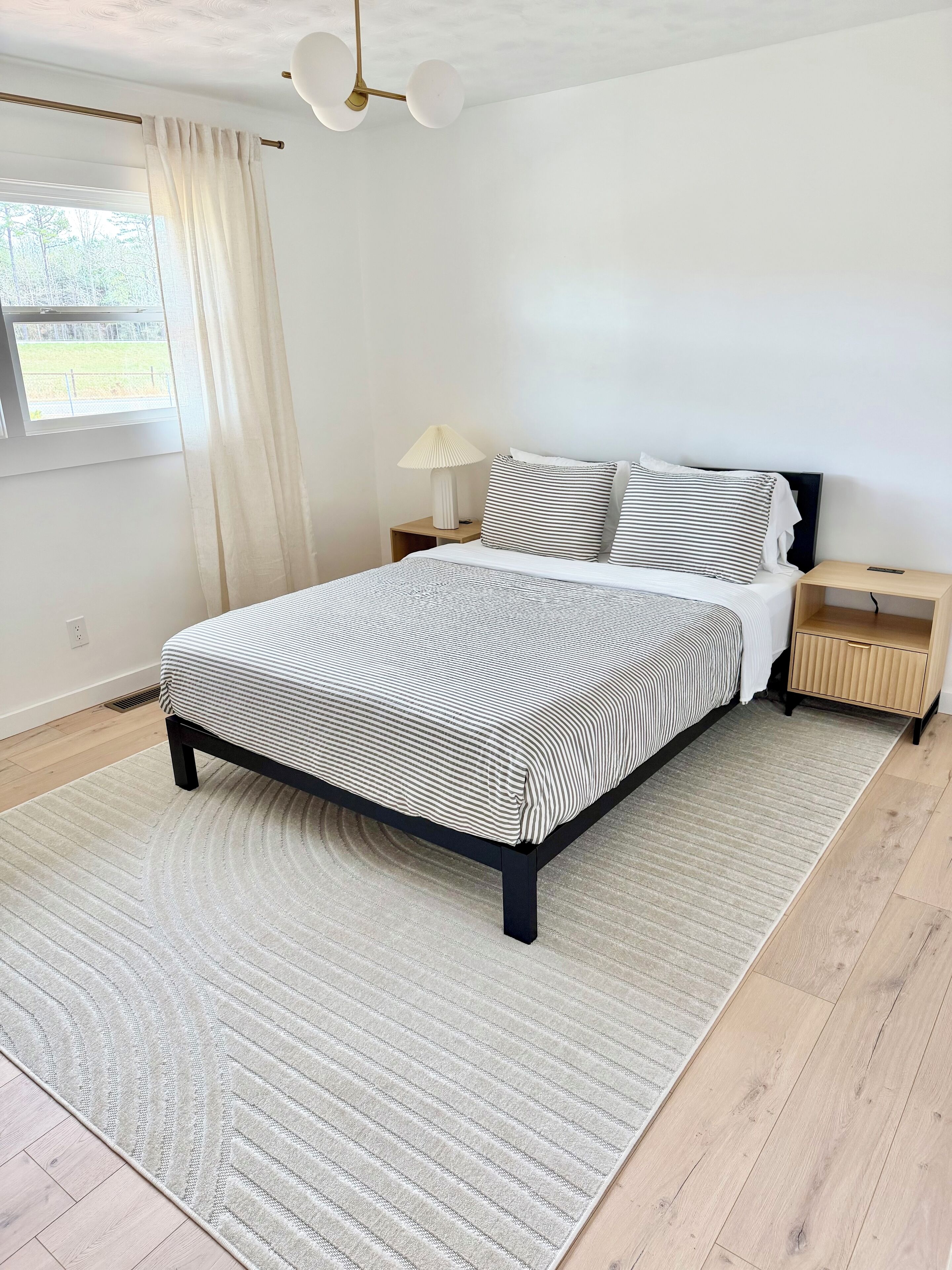 Een moderne slaapkamer met een bed, nachtkastjes, een lamp en uitzicht op het omliggende landschap.