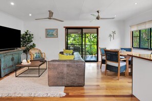 Ein modernes Wohnzimmer mit Sofa, Couchtisch und Sesseln, einem Fernseher und Blick auf Grün hinter einer Schiebetür.