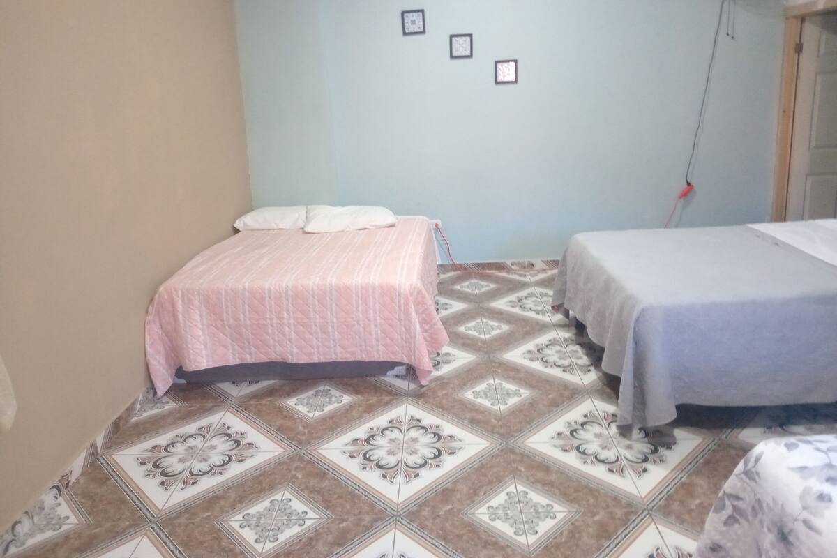 A bedroom with two beds, patterned floor tiles, and a wall-mounted fan.