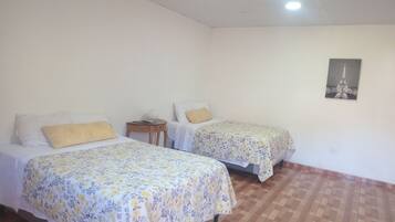 A room with two beds, each with floral bedspreads, a small wooden nightstand, and a wall-mounted picture.