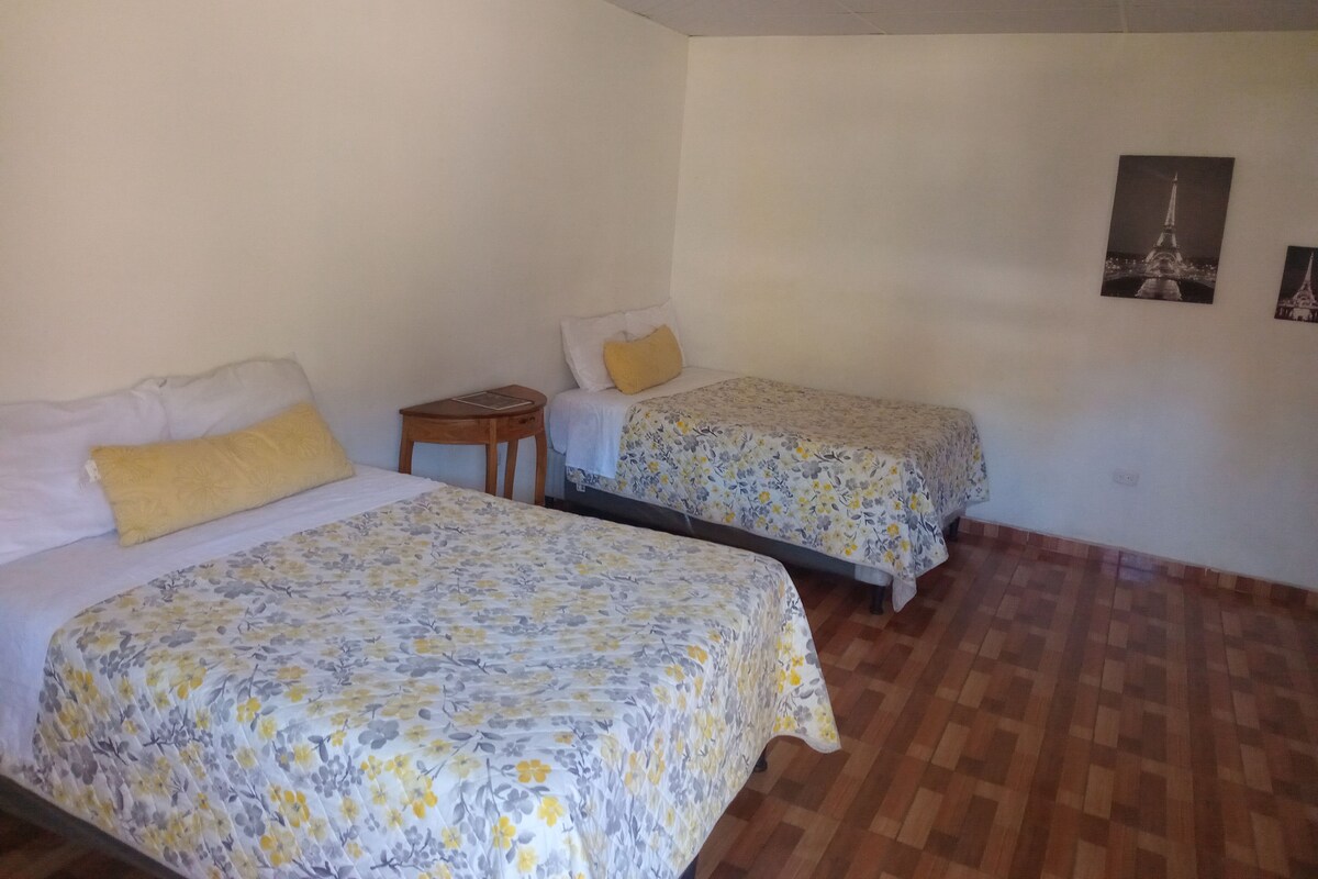 A room with two beds, wooden flooring, and a small table.