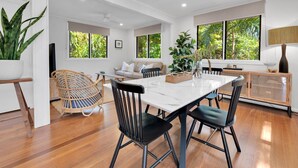 A modern dining area with a white marble table, black chairs, and a wooden floor. - Birdwing Retreat (Picnic Bay)