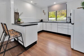 Cozinha moderna com armários brancos, bancada preta e piso de madeira.