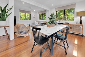 Un espace repas moderne avec une table en marbre blanc, des chaises noires et un plancher en bois.