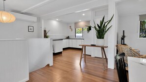 A modern kitchen with white cabinetry, a wooden floor, a hanging light fixture, and a potted plant. - Birdwing Retreat (Picnic Bay)
