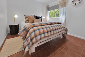 Un dormitorio con cama, una lámpara de noche, una ventana con cortinas y una mesita redonda.