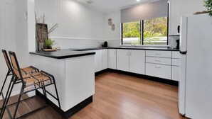 A modern kitchen with white cabinetry, a black countertop, and a wooden floor. - Birdwing Retreat (Picnic Bay)