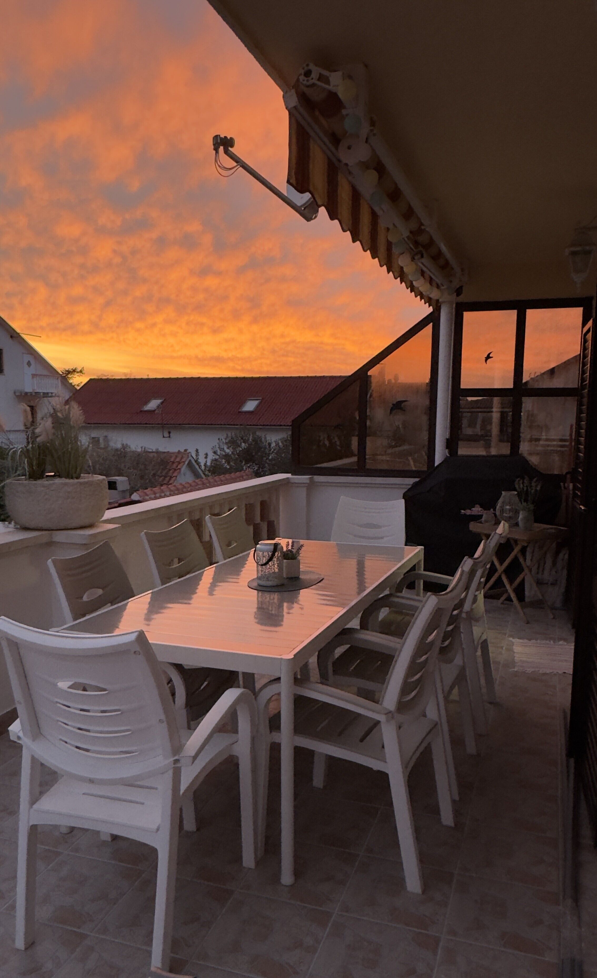An outdoor dining area with a table and chairs, a pergola, and a view of the sunset.