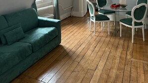 Ett modernt vardagsrum med en grön soffa, ett glasbord med vita stolar, en golvlampa och ett element.