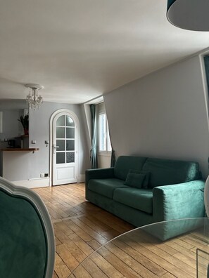 A spacious living room with a green sofa, wooden flooring, a white door, and a chandelier. - Central Splendid Apartment Louvre 1st District Paris (Paris)