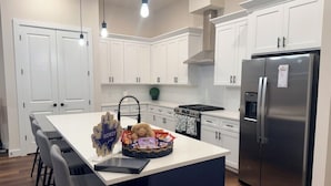 Una cocina moderna con armarios blancos, un refrigerador de acero inoxidable y una isla central con taburetes de bar.