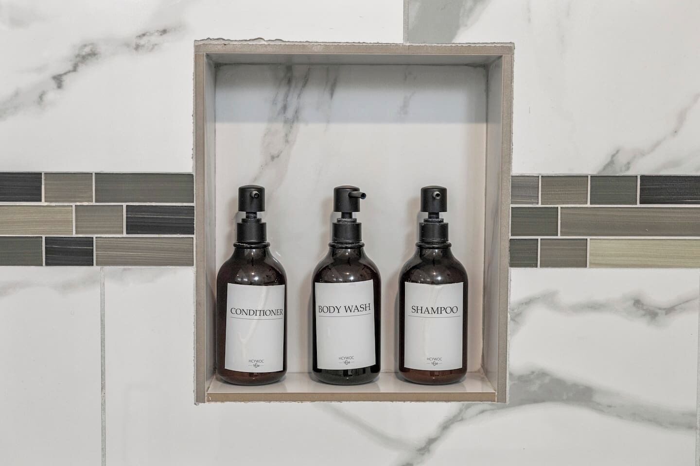 Un estante de baño con tres botellas de productos para el cuidado de la piel: acondicionador, gel de baño y champú.
