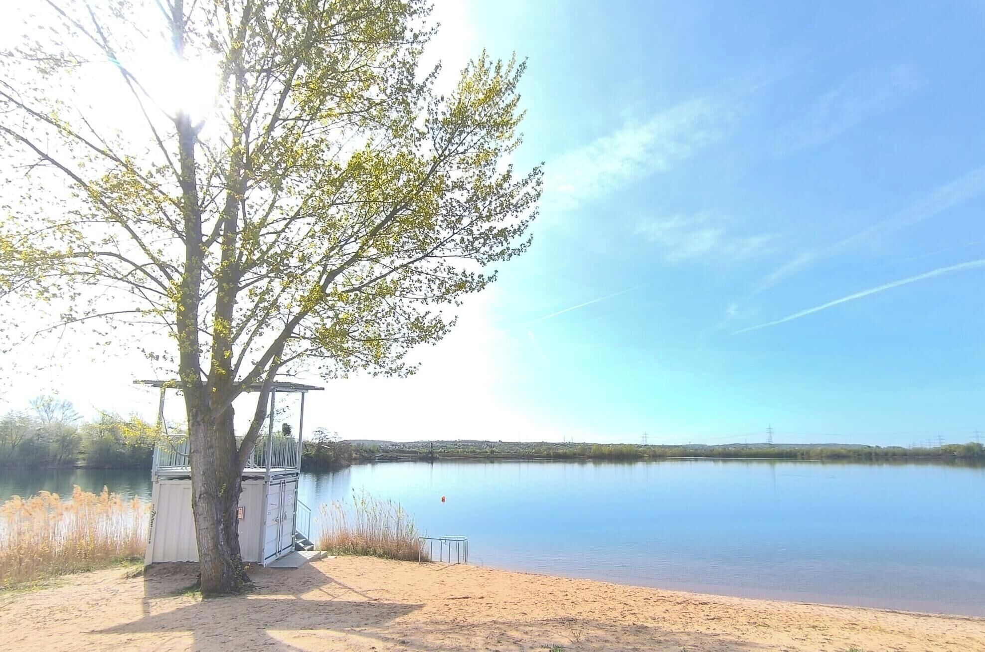 Ein ruhiger See mit einem Baum und einer kleinen Bausubstanz am Ufer.
