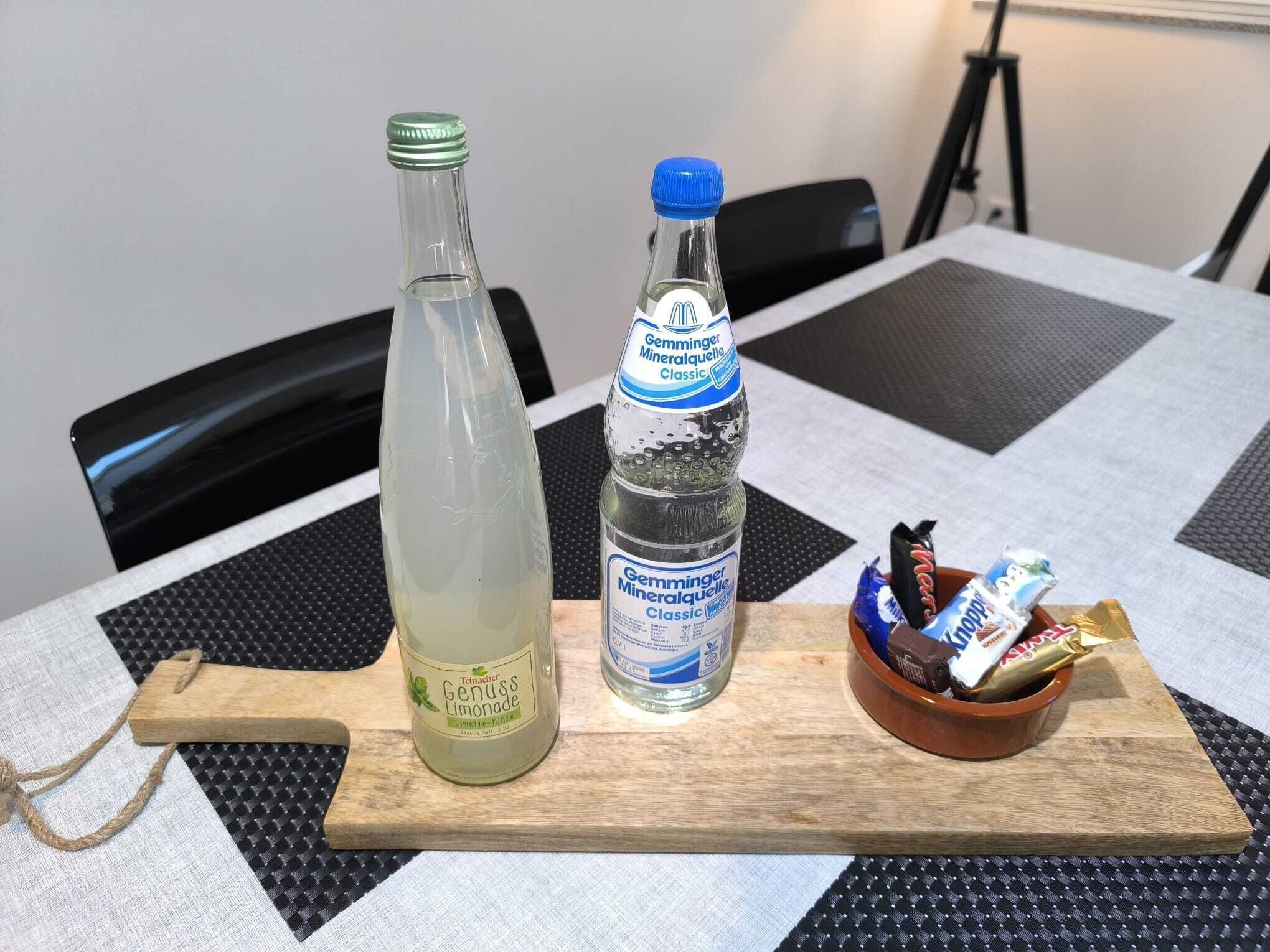 Ein Tisch mit einer Flasche Zitronenlimonade, einer Flasche Mineralwasser und einer Schüssel Snacks.