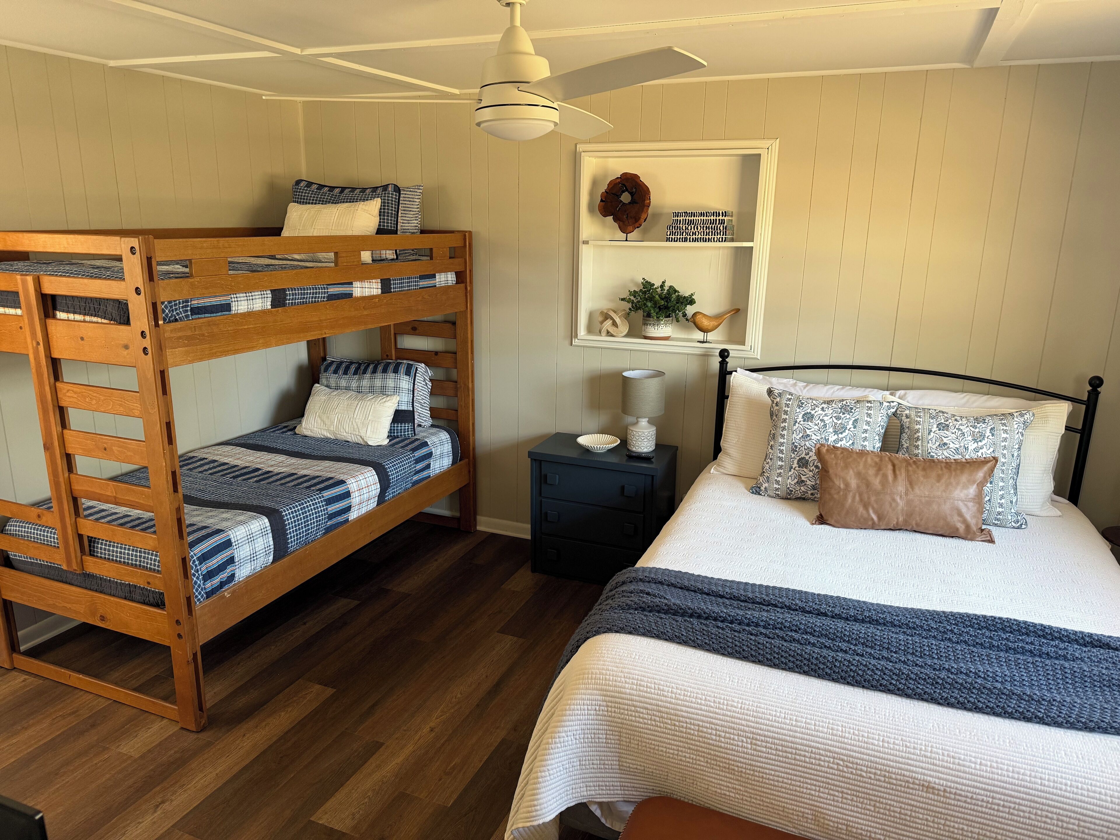 A bunk bed with a matching headboard, a bedside table with a lamp, and a large bed with patterned pillows.