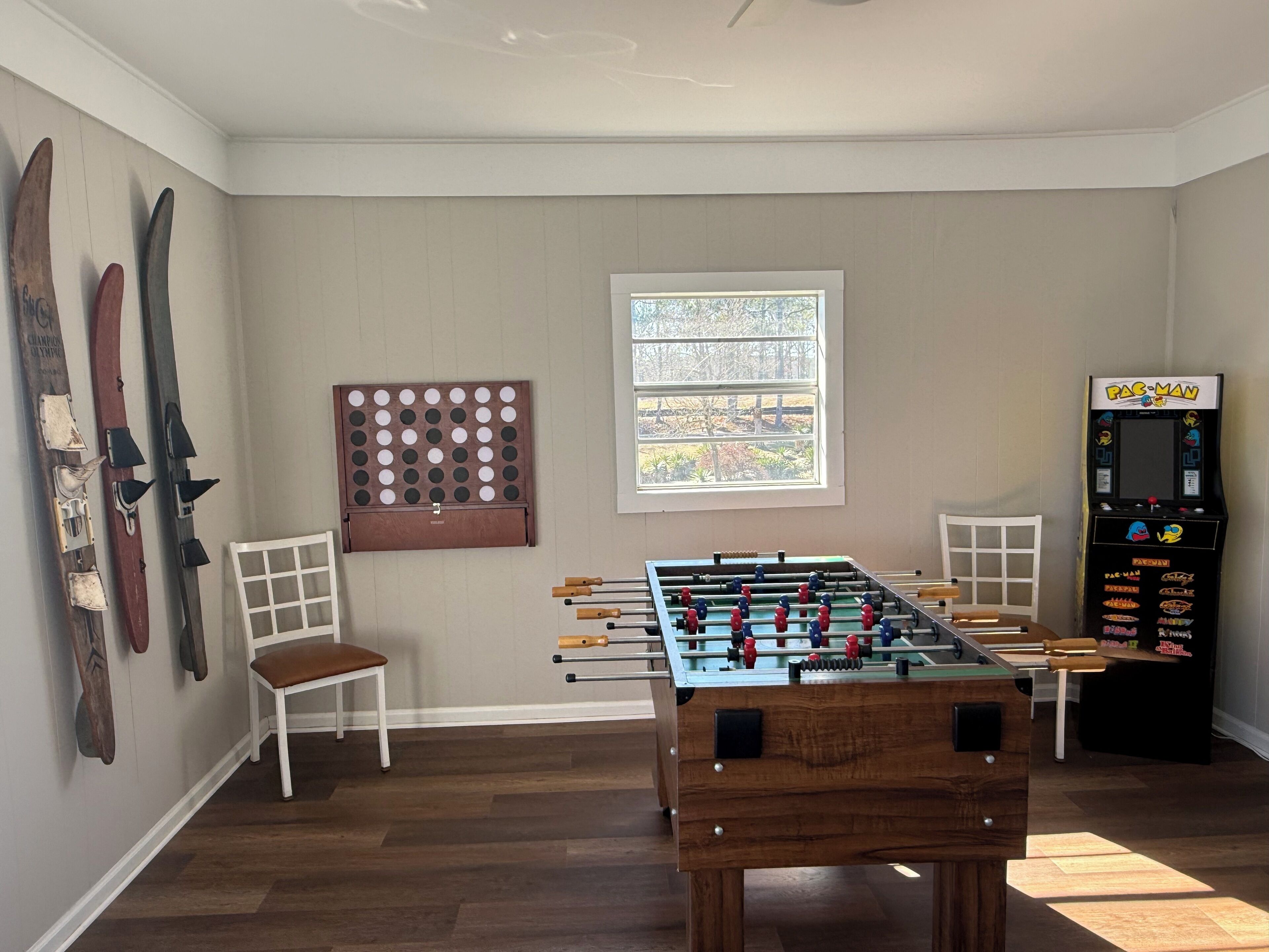 A room with a foosball table, a Pac-Man arcade machine, and skis on the wall.