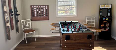 A room with a foosball table, a Pac-Man arcade machine, and skis on the wall.