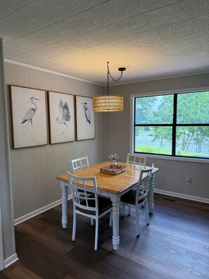 A dining room with a wooden table, white chairs, and three wall-mounted paintings of birds. - Weiss Choice - NEW RENTAL -charming lake house with stunning views (Leesburg)