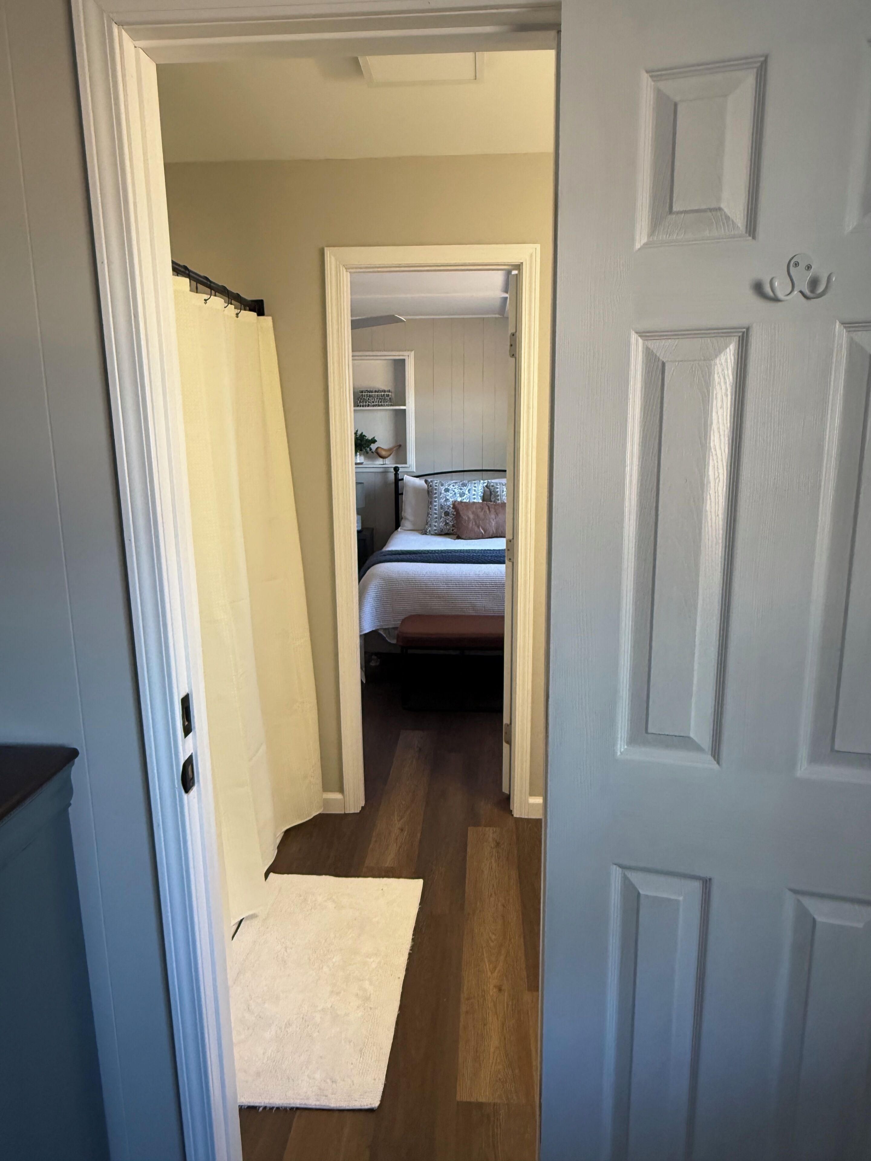 A narrow hallway leading to a bedroom with a bed, a nightstand, and a shelf with decorative items.