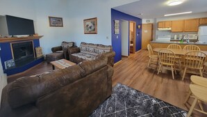 A living room with a brown leather sofa, a flat-screen TV, and a fireplace. There is a dining area with wooden chairs and a kitchen with wooden cabinets and a microwave. - LAKEFRONT 5-bedroom Chateau Getaway at Whitecap Mountains Resort Units 1 & 3 (Upson)