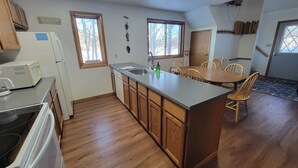 A kitchen with wooden cabinets, a central island, and a dining area with chairs. - LAKEFRONT 5-bedroom Chateau Getaway at Whitecap Mountains Resort Units 1 & 3 (Upson)