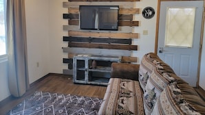 A living room with a mounted TV, a patterned sofa, and a rustic wooden wall. - LAKEFRONT 5-bedroom Chateau Getaway at Whitecap Mountains Resort Units 1 & 3 (Upson)