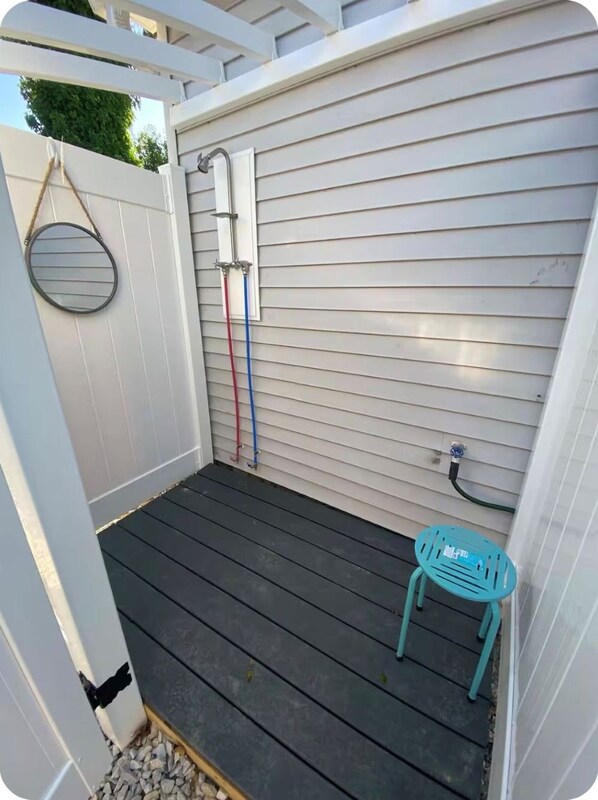 Een overdekte patio met een houten terras, een metalen stoel en een slang aangesloten op een kraan op de muur.