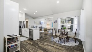 Een moderne keuken met witte kasten, een roestvrijstalen koelkast en een eetgedeelte met een ronde tafel en stoelen.