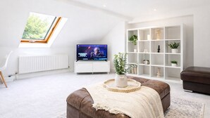 Ett modernt vardagsrum med en TV, en vit hylla, en brun lädersoffa och ett takfönster.