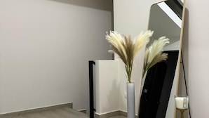 Una camera moderna con un grande specchio, un'alta composizione floreale con pampas e un diffusore nero.