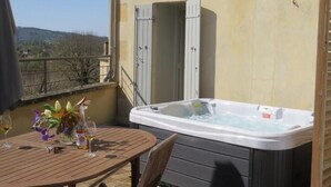 Uma banheira de hidromassagem numa varanda, com mesa, cadeiras, um arranjo de flores e vista para as colinas.