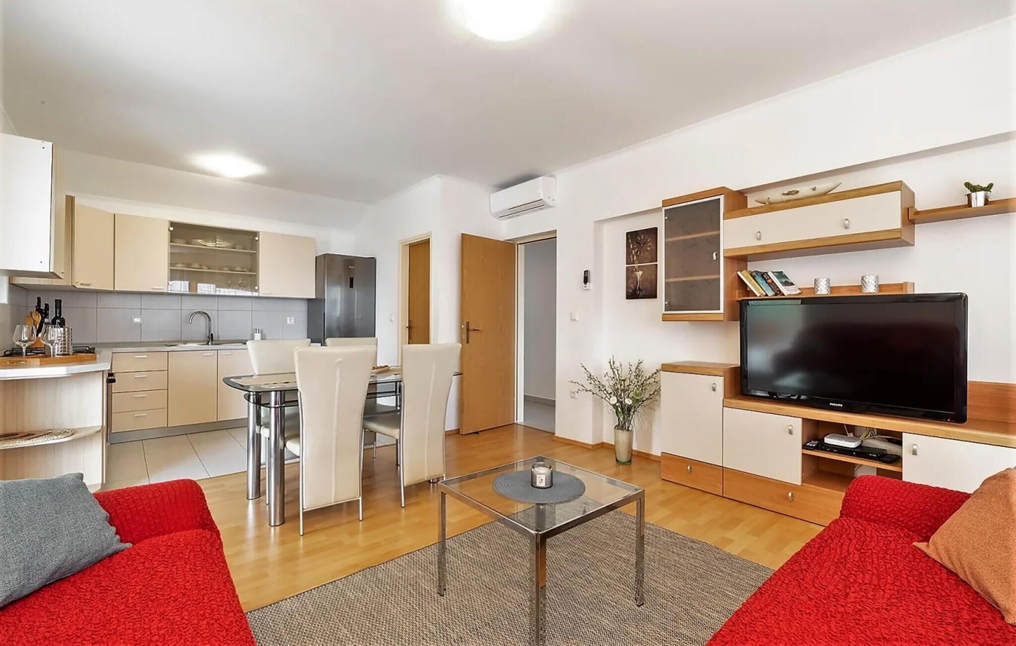 A modern apartment with a kitchen, dining area, and living room. It includes a flat-screen TV, a coffee table, and red sofas.