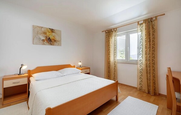 A bedroom with a wooden bed, two bedside tables, a desk, and a window with curtains.
