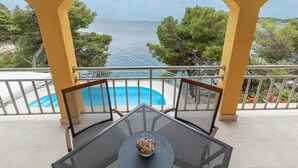 Een balkon met uitzicht op zee, een zwembad en terrasmeubels.