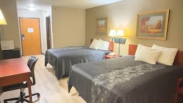 A hotel room with two beds, a desk, and a chair. There are two lamps on the desk and a door in the background.