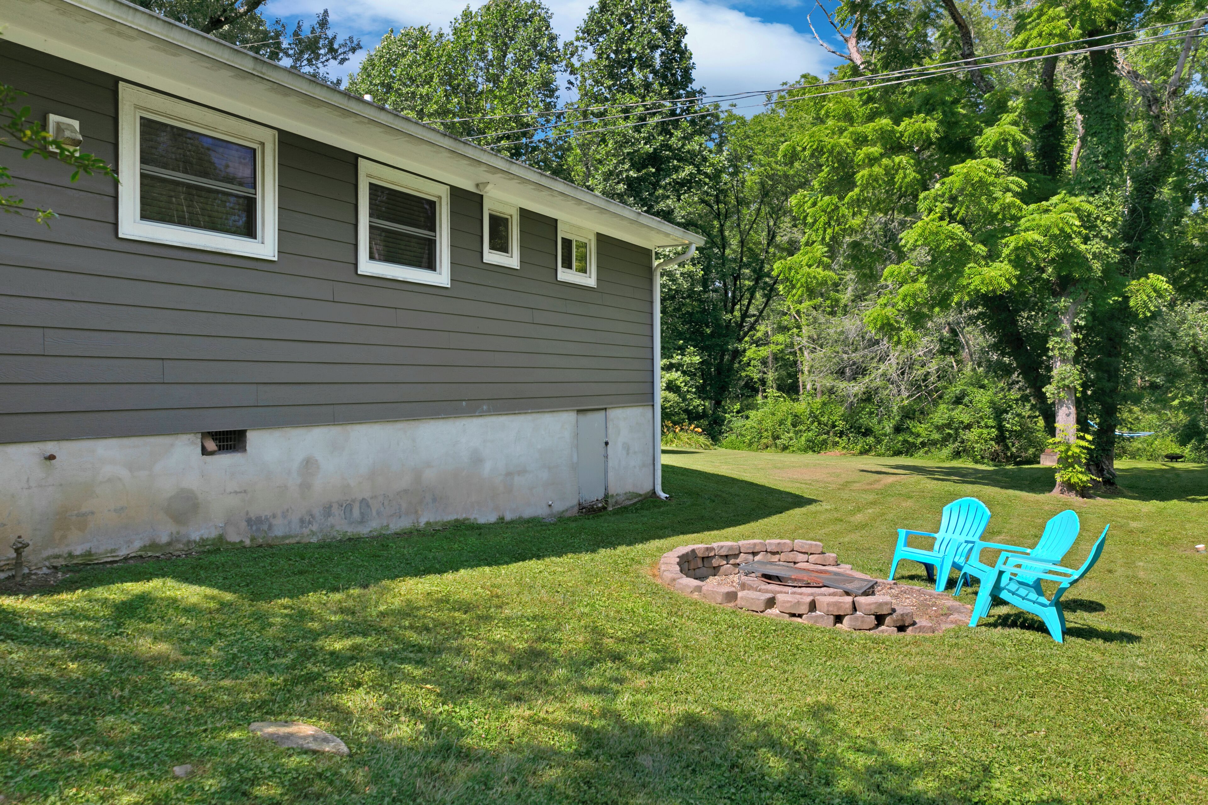 A house with a grey exterior, a small front yard, and a fire pit area with two blue Adirondack chairs.