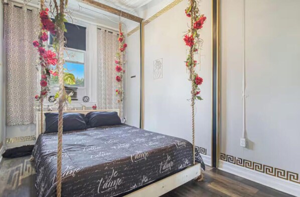 A bedroom with a four-poster bed, a window with patterned curtains, and a wall with a geometric border.